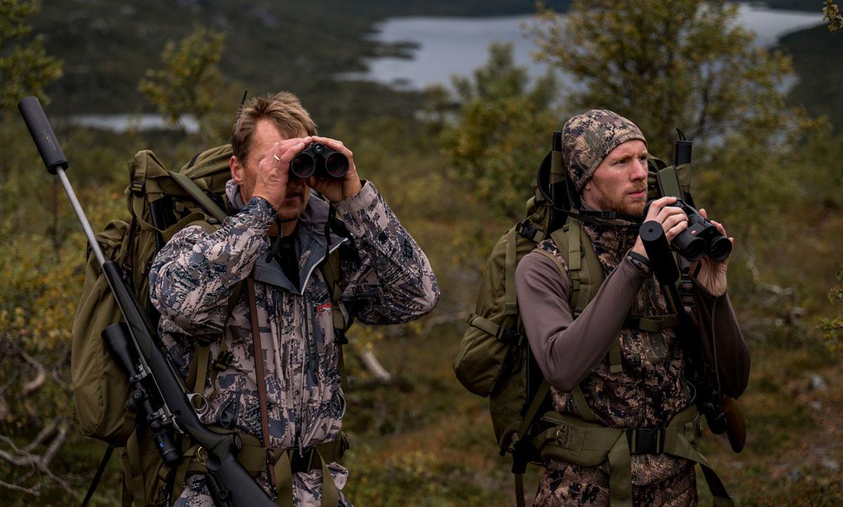 Zwei Jäger in Tarnkleidung schauen mit Ferngläsern nach Rentieren