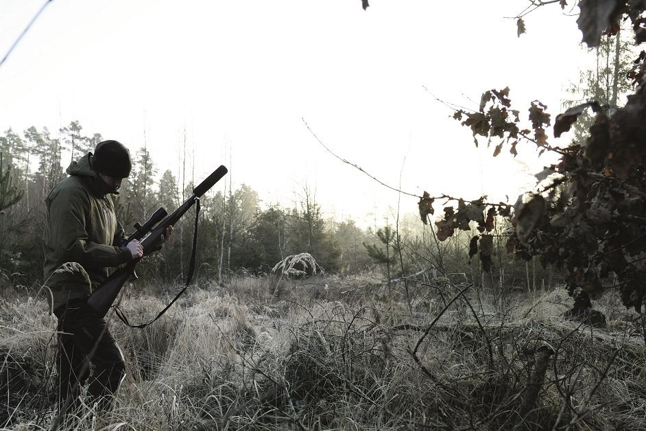 Jäger steht mit Gewehr und Schalldämpfer im Wald